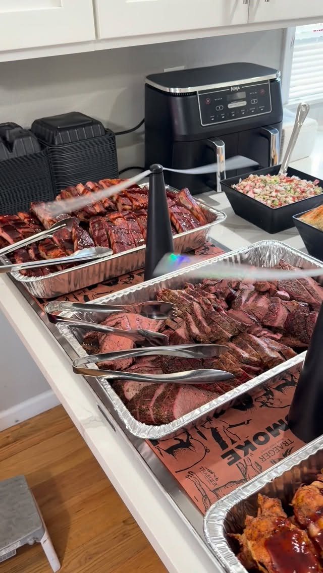 Sliced smoked brisket and ribs in aluminum trays on a white buffet counter.