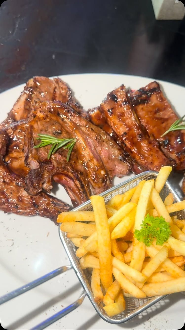 Glazed grilled ribs and french fries served on a white plate with rosemary.