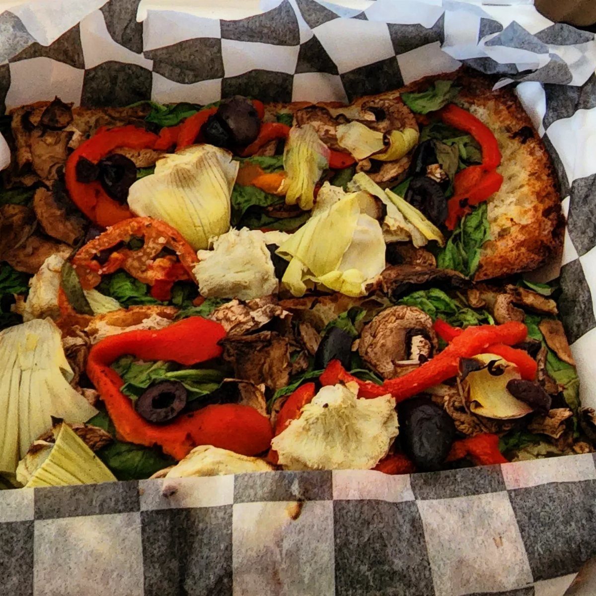 Vegetable pizza with red peppers and artichokes in a checkered paper basket
