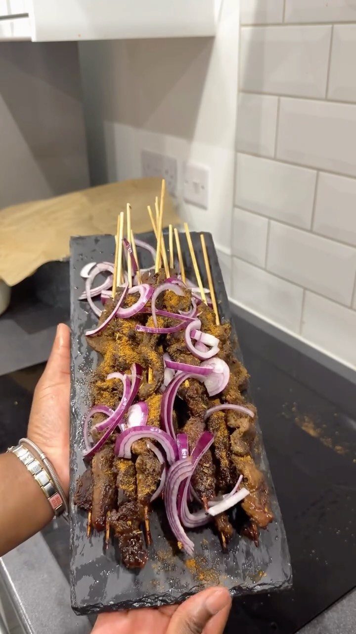 Grilled meat skewers with red onion slices on a black slate platter.