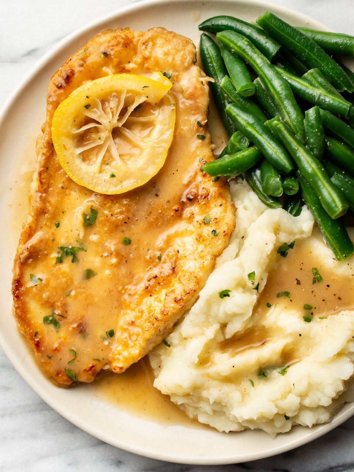 Seared chicken breast with lemon slice, mashed potatoes, and steamed green beans.