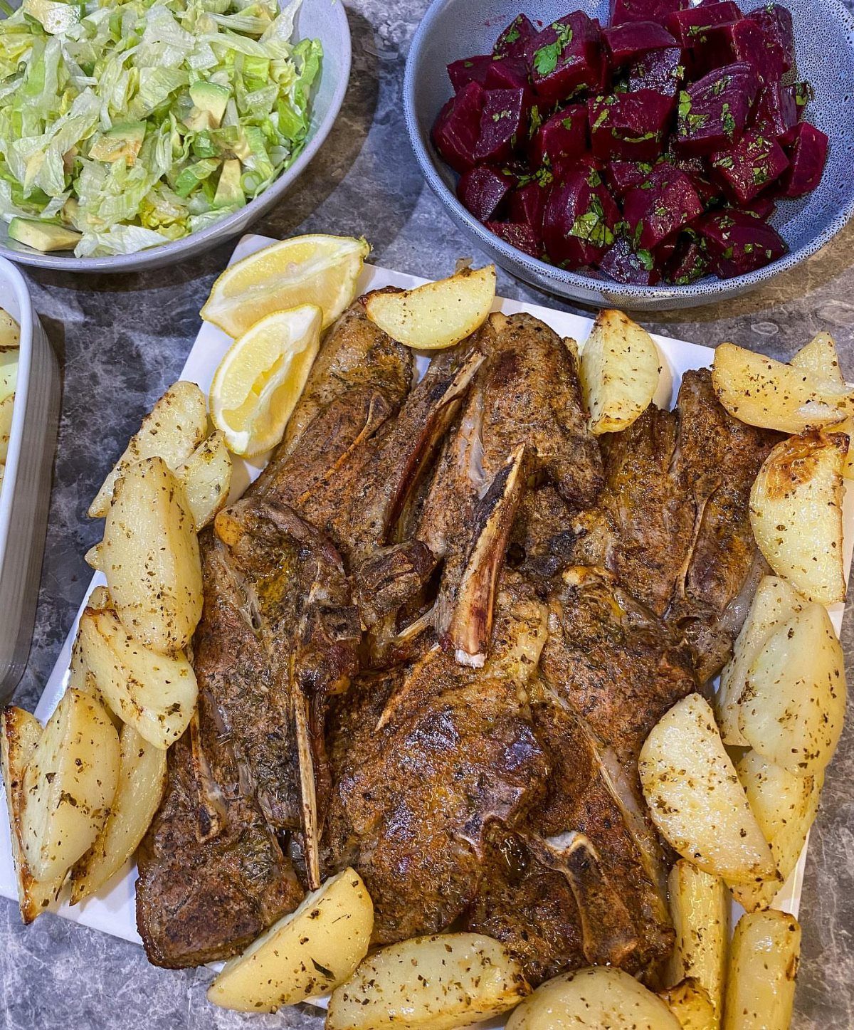 Grilled lamb chops with roasted potato wedges and lemon on a white platter.