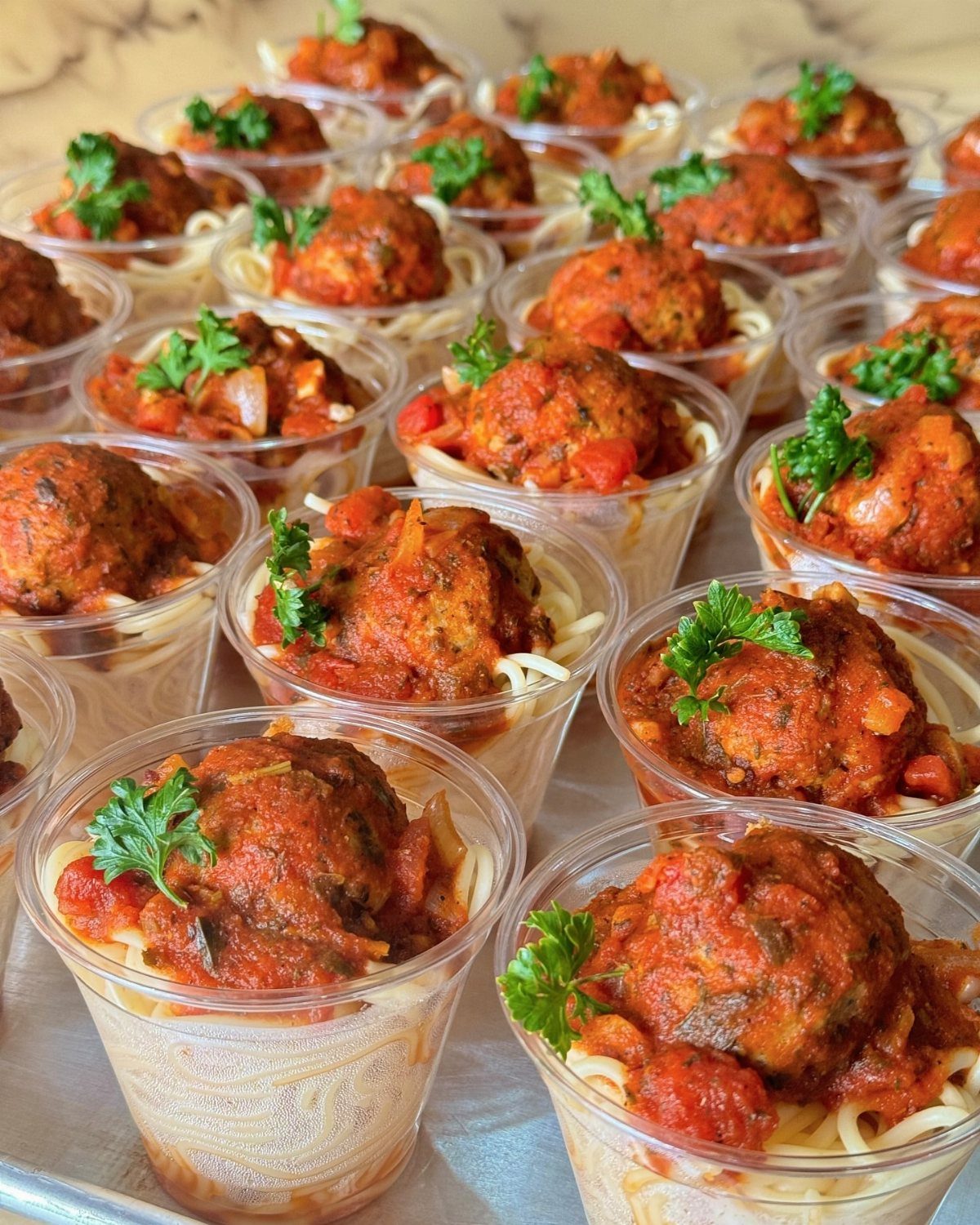 Meatballs in tomato sauce over spaghetti served in individual clear plastic appetizer cups.