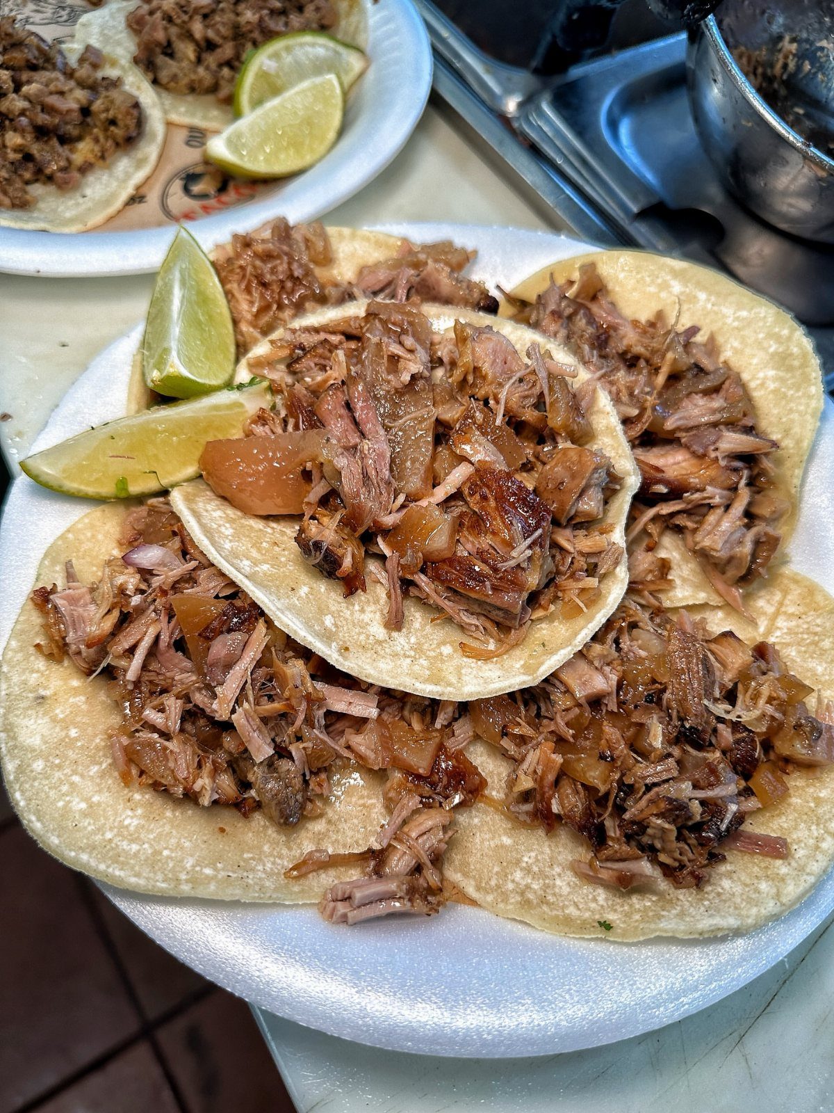 Shredded pork carnitas tacos on corn tortillas with fresh lime wedges on a plate.