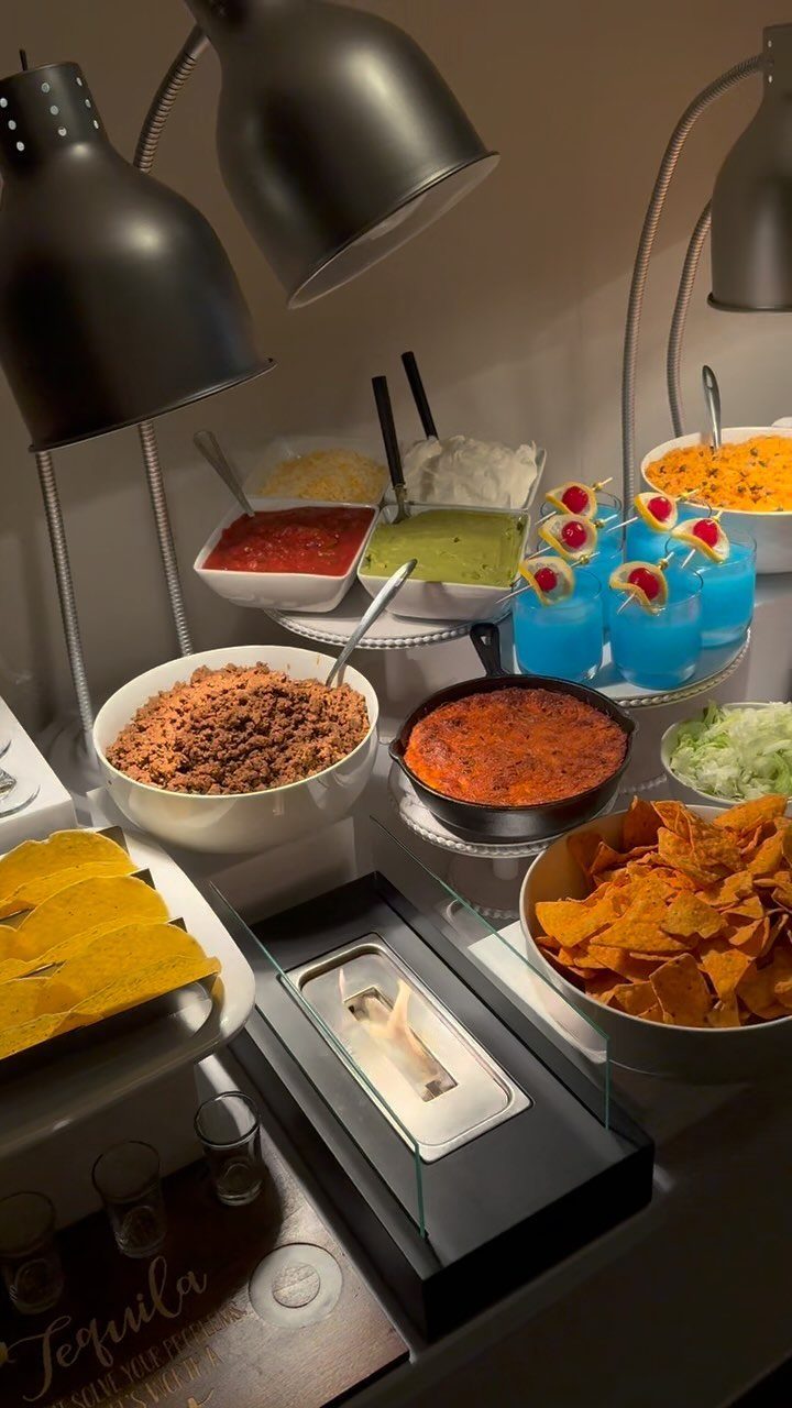 Taco bar buffet with ground meat, salsas, tortilla chips, and blue cocktails.