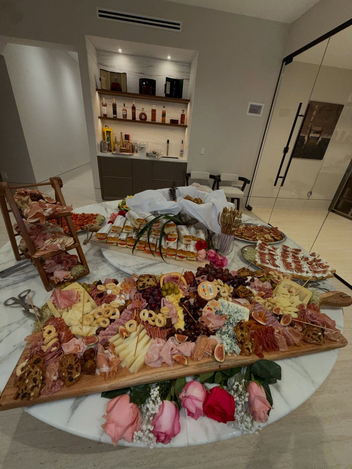 Large charcuterie board and appetizer platters arranged on a white marble table.