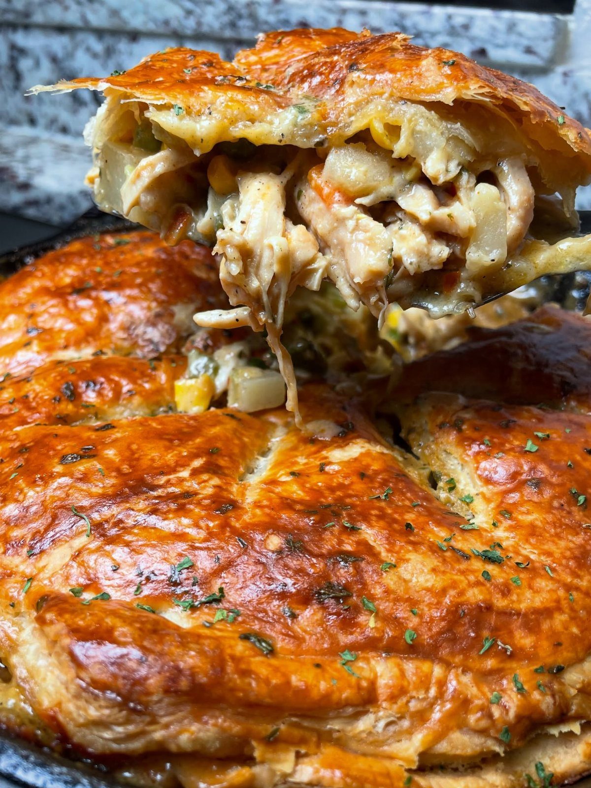 Chicken pot pie with golden flaky crust and creamy vegetable filling being lifted.