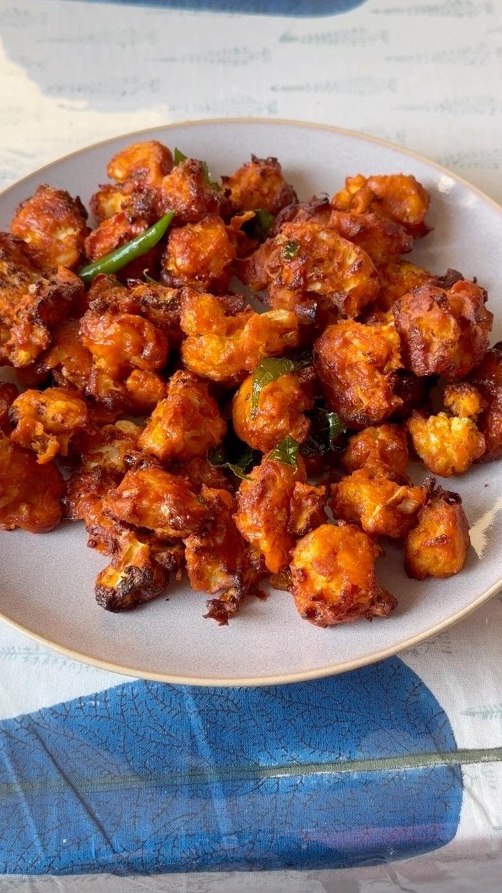 Seasoned cauliflower florets with green chilies served on a white ceramic plate.