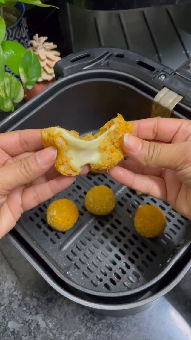 Fried cheese balls in an air fryer with one being pulled apart.