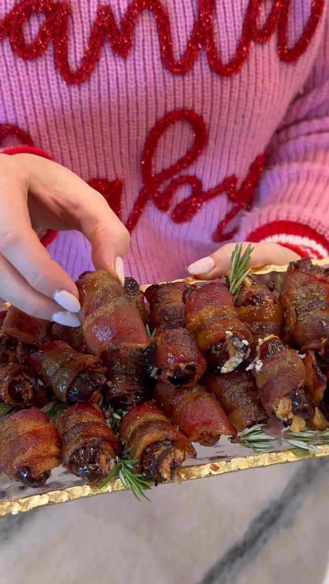 Bacon-wrapped dates on a gold platter held by a person in a pink sweater.
