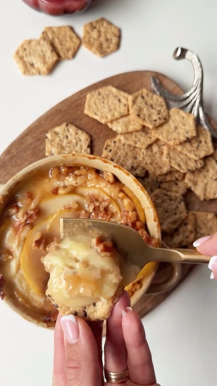 Melted baked brie with pears being scooped onto a hexagonal cracker.