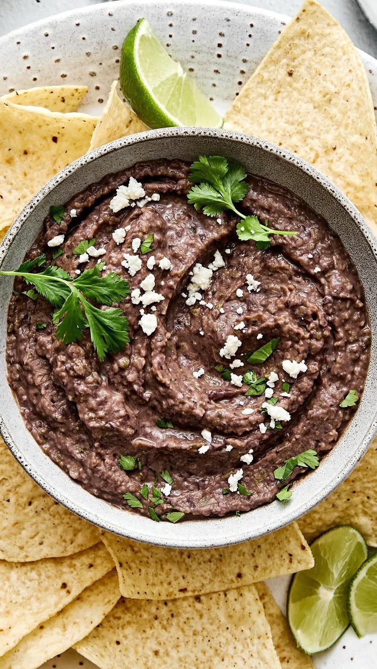 Black bean dip topped with cheese and cilantro, served with tortilla chips and lime.