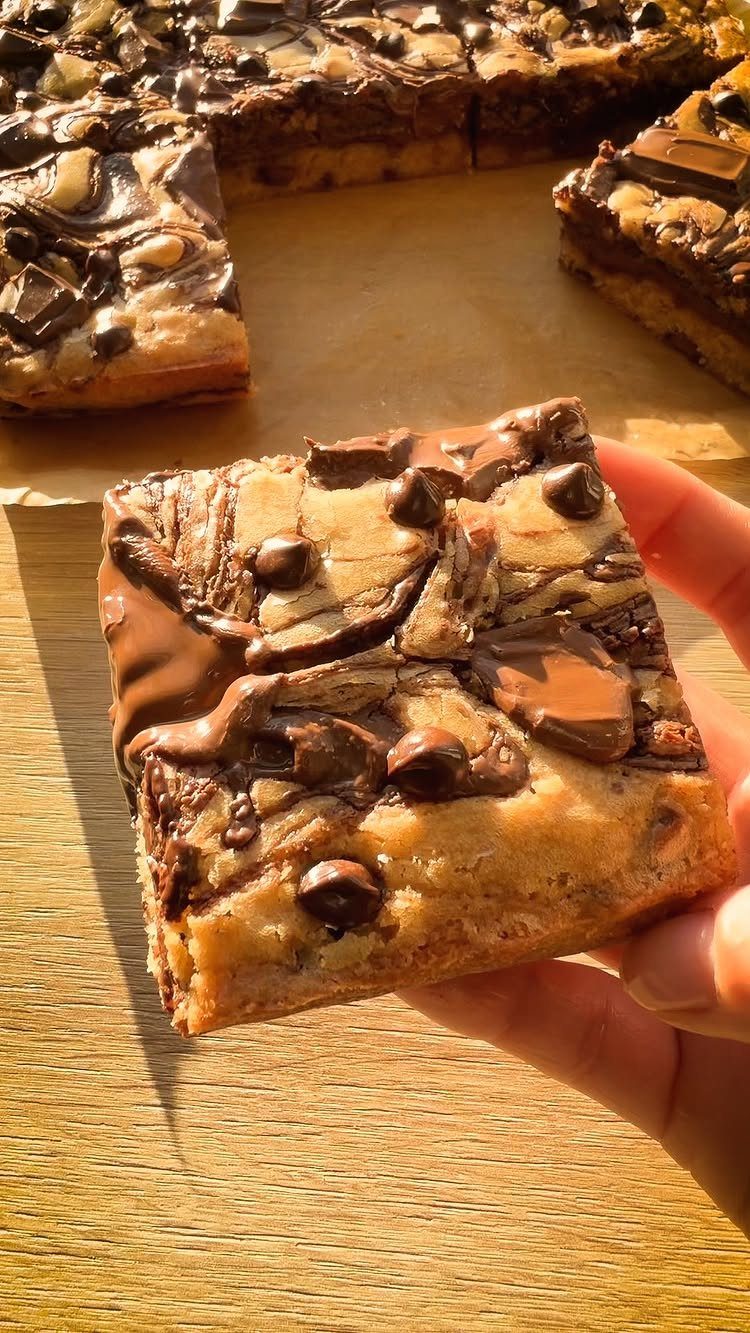 Chocolate chip blondie bar held in a hand over more bars on parchment.
