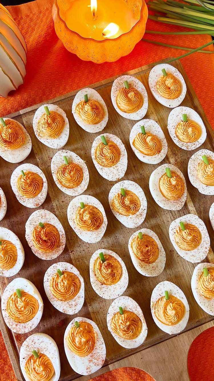 Deviled eggs with orange pumpkin-shaped filling arranged on a wooden serving board.