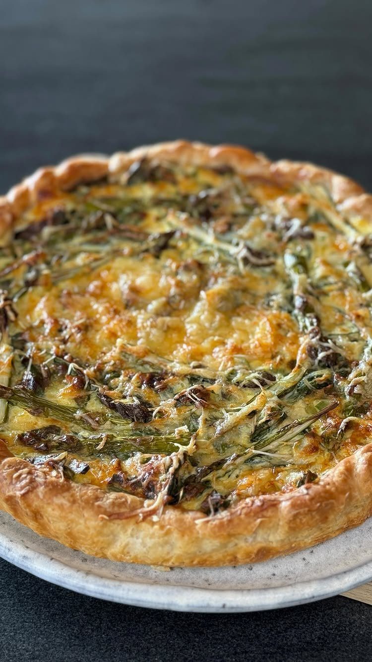 Savory tart with melted cheese and asparagus on a light-colored plate.