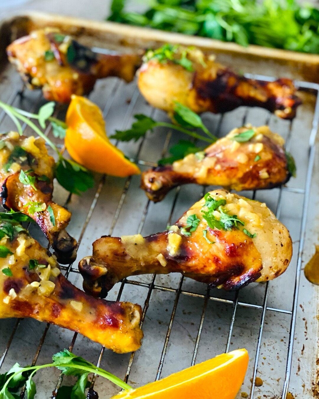 Glazed chicken drumsticks with garlic and parsley on a wire cooling rack.