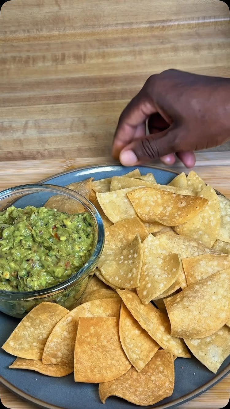 Guacamole in a glass bowl served with corn tortilla chips on a plate.