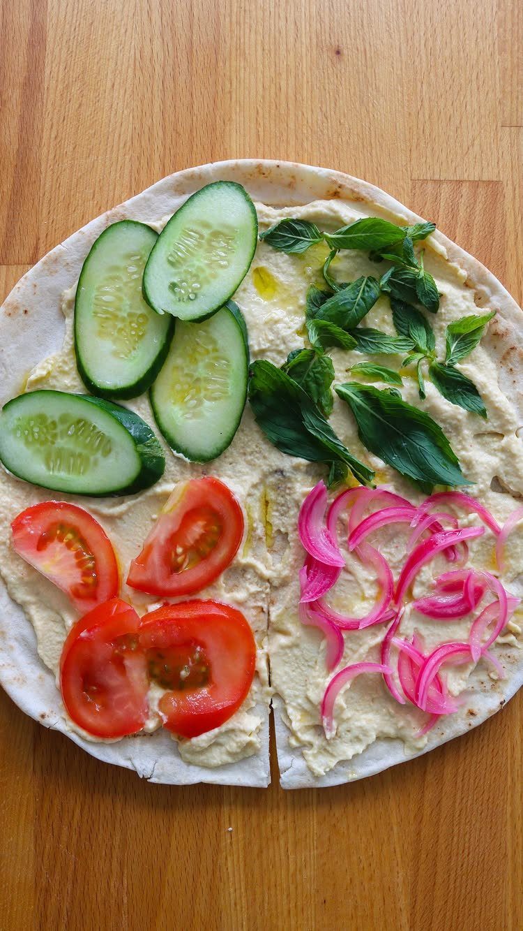 Hummus topped pita bread with cucumbers, tomatoes, basil, and pickled red onions.