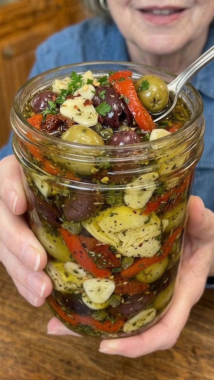 Marinated green and purple olives with garlic and peppers in a glass jar.