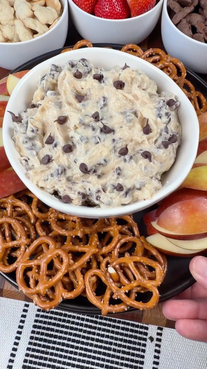 Creamy peanut butter dip with chocolate chips surrounded by pretzels and sliced apples.