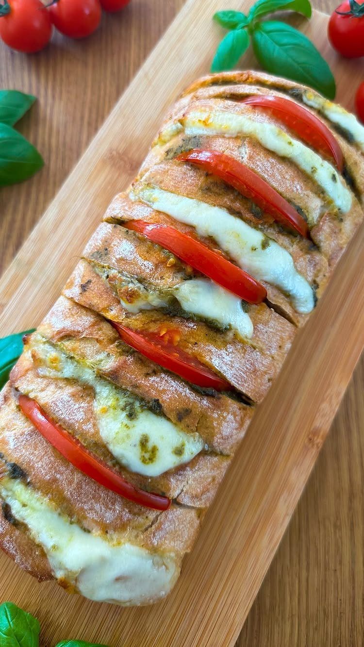 Pesto pull-apart bread with melted cheese and tomato slices on a wooden board.