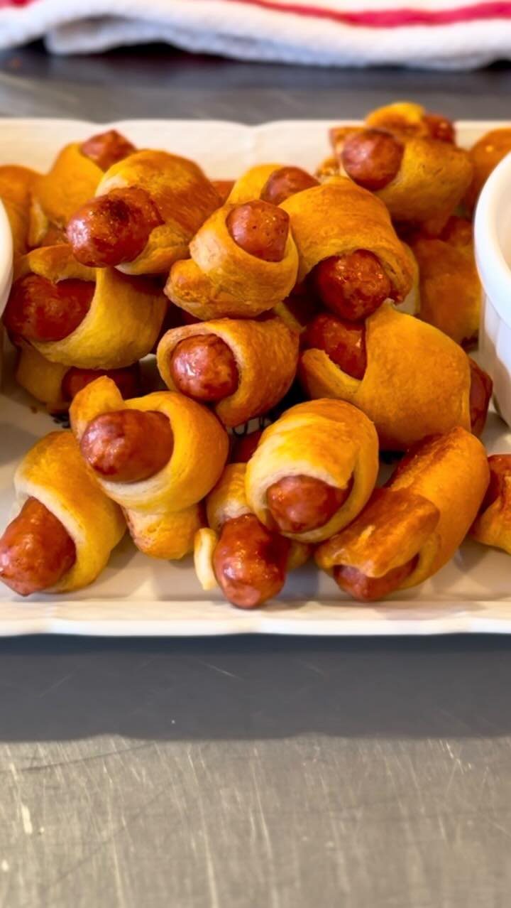 Small sausages wrapped in golden-brown pastry dough piled on a white platter.