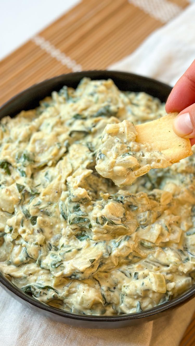 Spinach artichoke dip in a black skillet with a chip being dipped in.