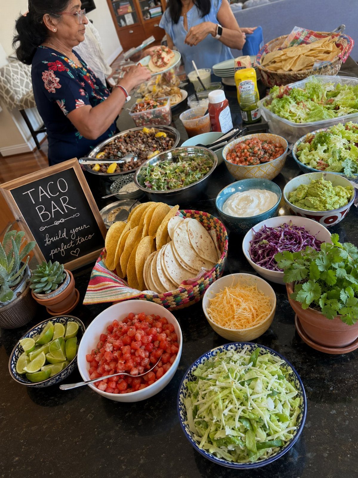 Taco bar spread with various toppings, tortillas, and a person assembling a taco.