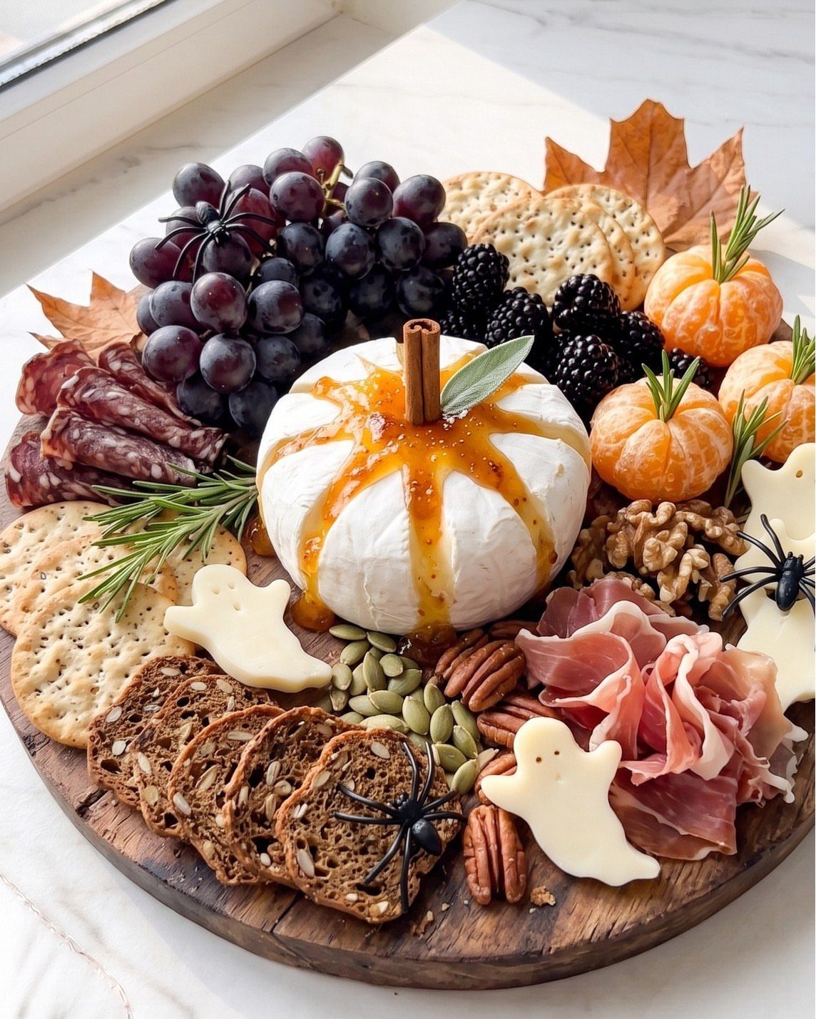Festive charcuterie board with pumpkin-shaped brie, ghost cheese, fruits, and assorted meats.