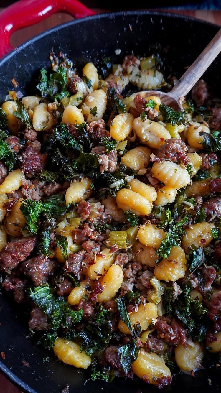 Gnocchi stuffing with sausage and kale in a black skillet with wooden spoon.