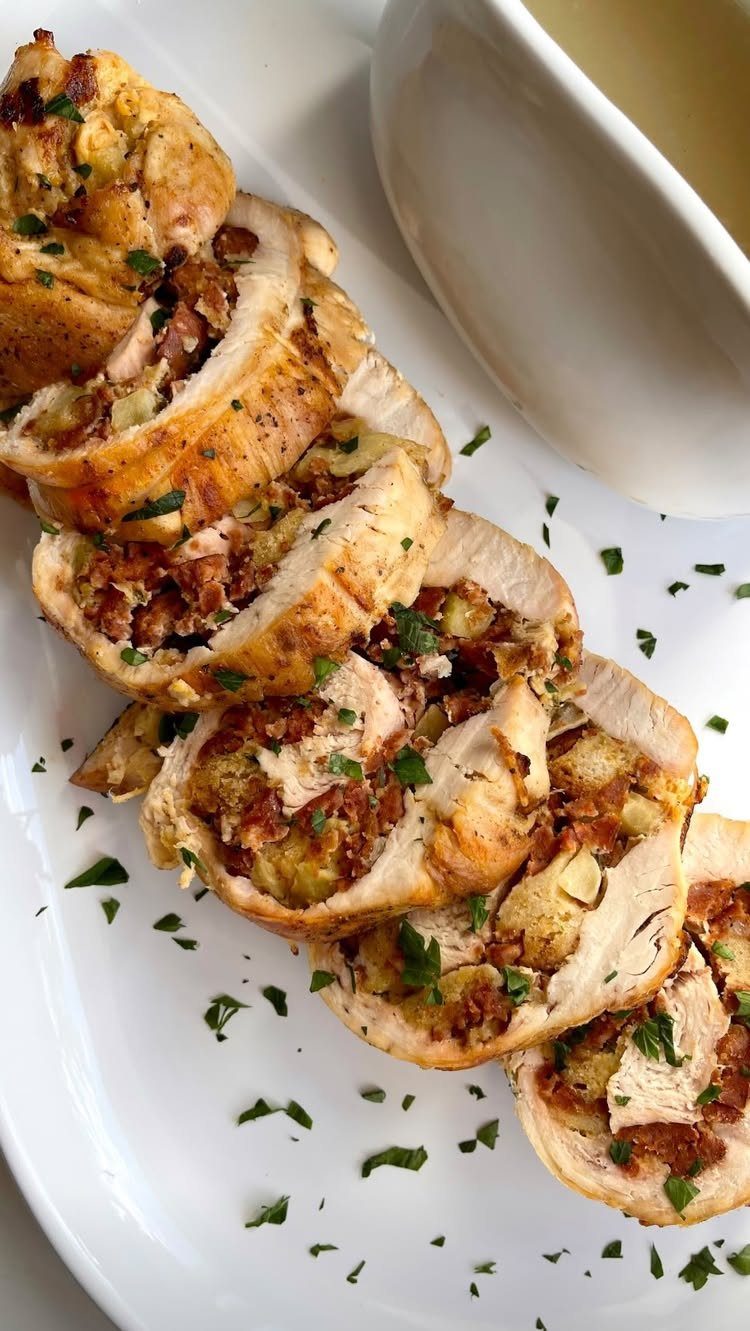 Slices of roasted stuffed turkey breast on a white platter with gravy bowl.