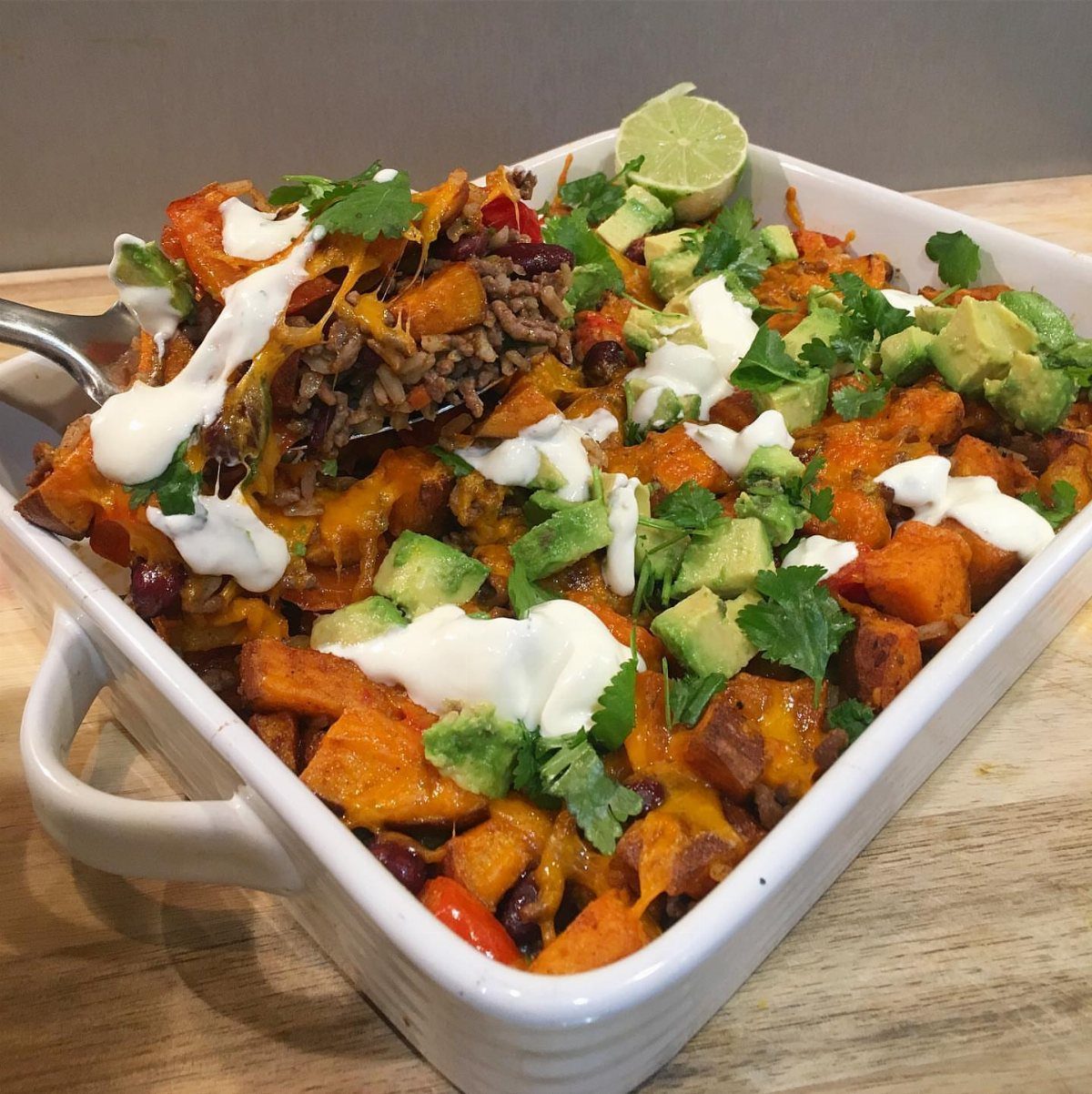 Sweet potato and black bean casserole topped with avocado, cream, and cilantro.