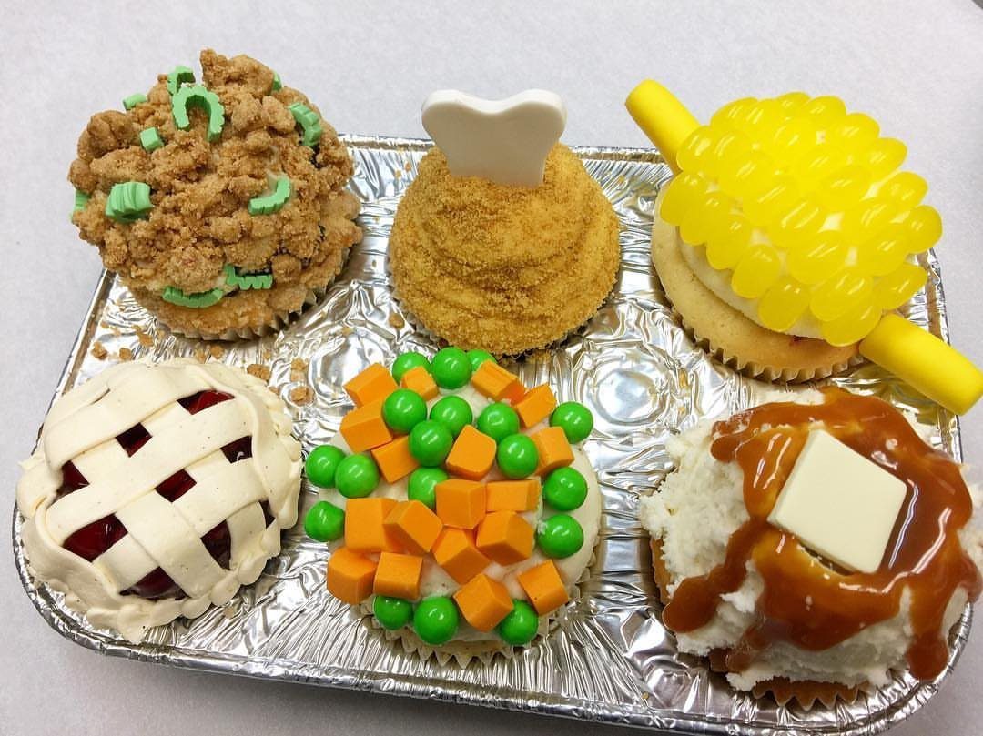 Six cupcakes decorated as Thanksgiving foods on a silver foil tray.