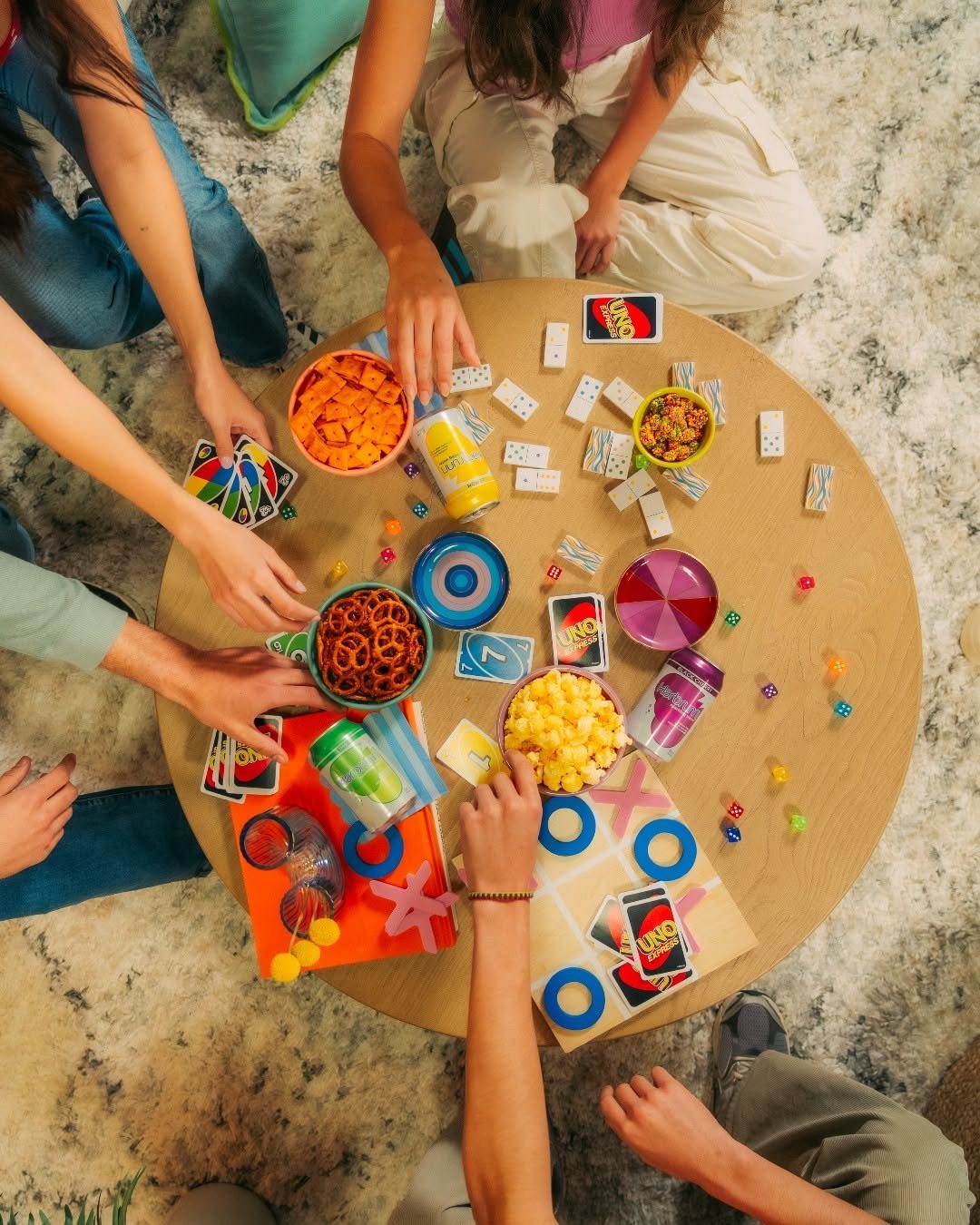 People playing card and board games around a table with various snack bowls.