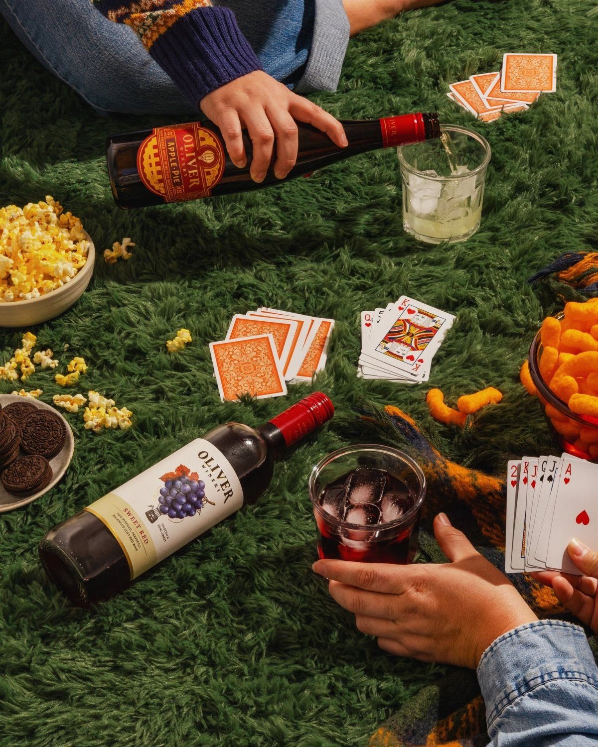 Playing cards, wine bottles, and bowls of snacks on a green shag rug.