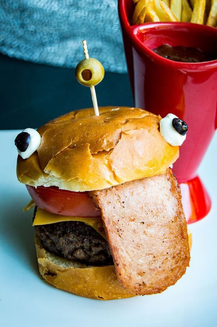 Monster-themed burger with a ham tongue and olive eye next to french fries