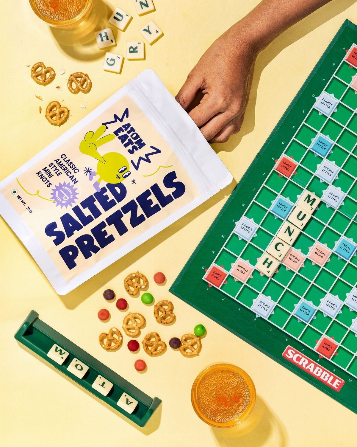 Scrabble board and salted pretzels with candies and drinks on a yellow background