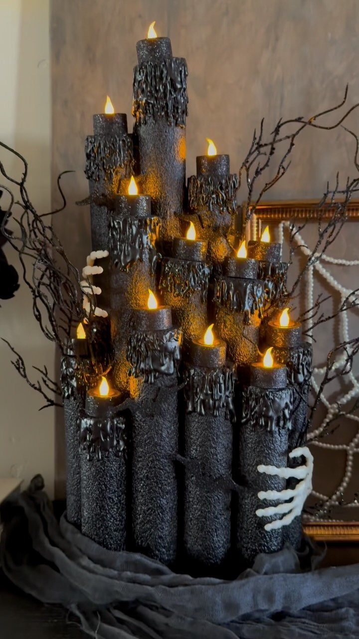 Black textured pillar candles with orange flames and skeleton hands among dark branches.