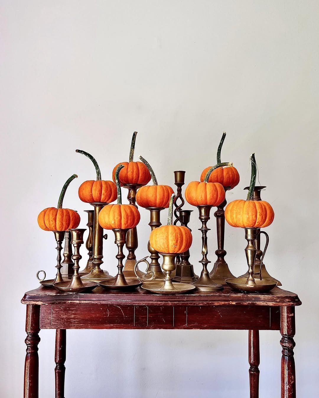 Small orange pumpkins perched on brass candlesticks atop a dark wooden table.