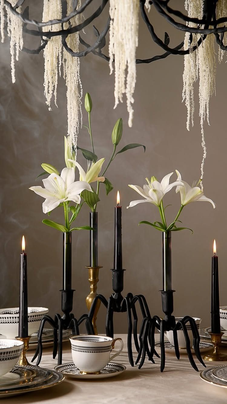 White lilies in black claw-shaped vases with black candles on a table.