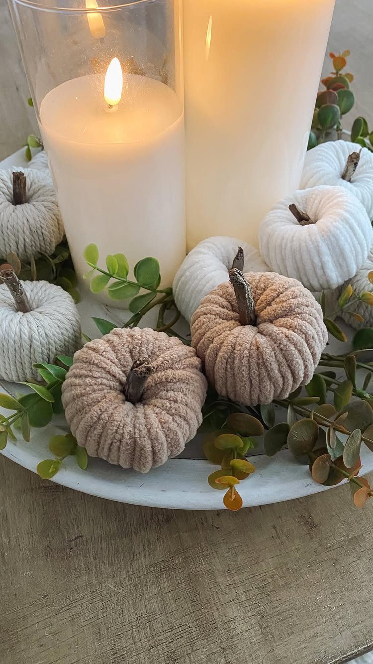 Fabric pumpkins in neutral tones arranged with white candles and eucalyptus on marble.
