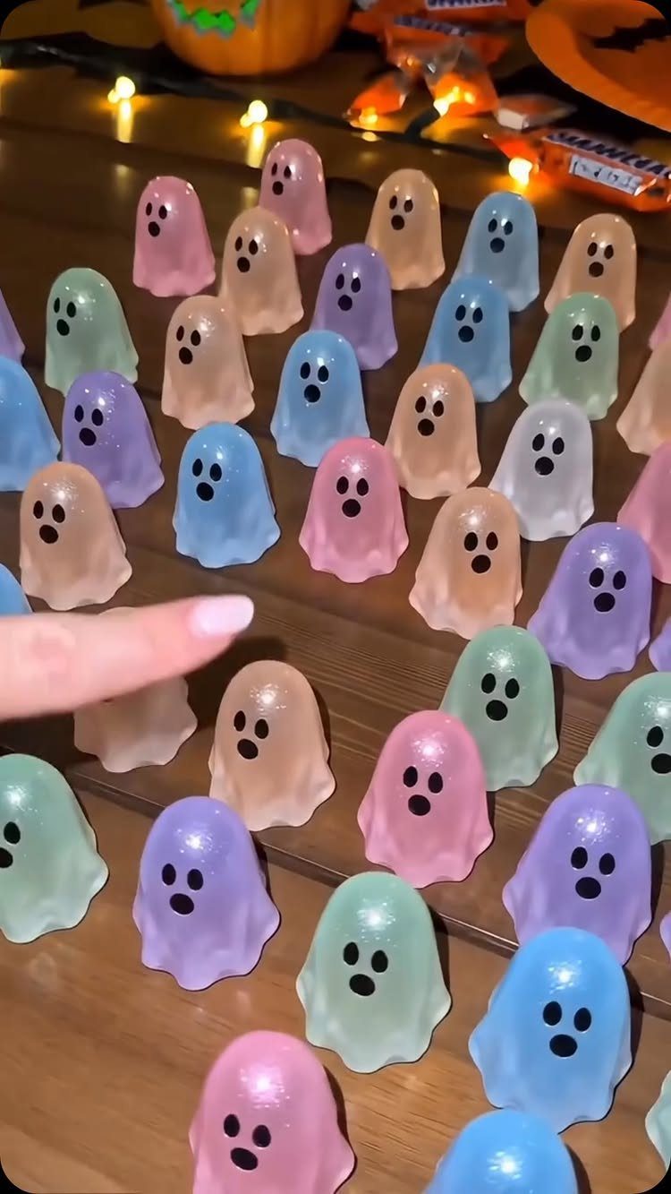 Colorful translucent ghost figurines arranged on a wooden table with Halloween candy.