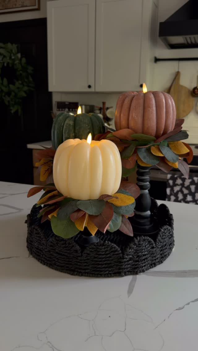 Pumpkin shaped candles on black pedestals with autumn leaves on a woven mat