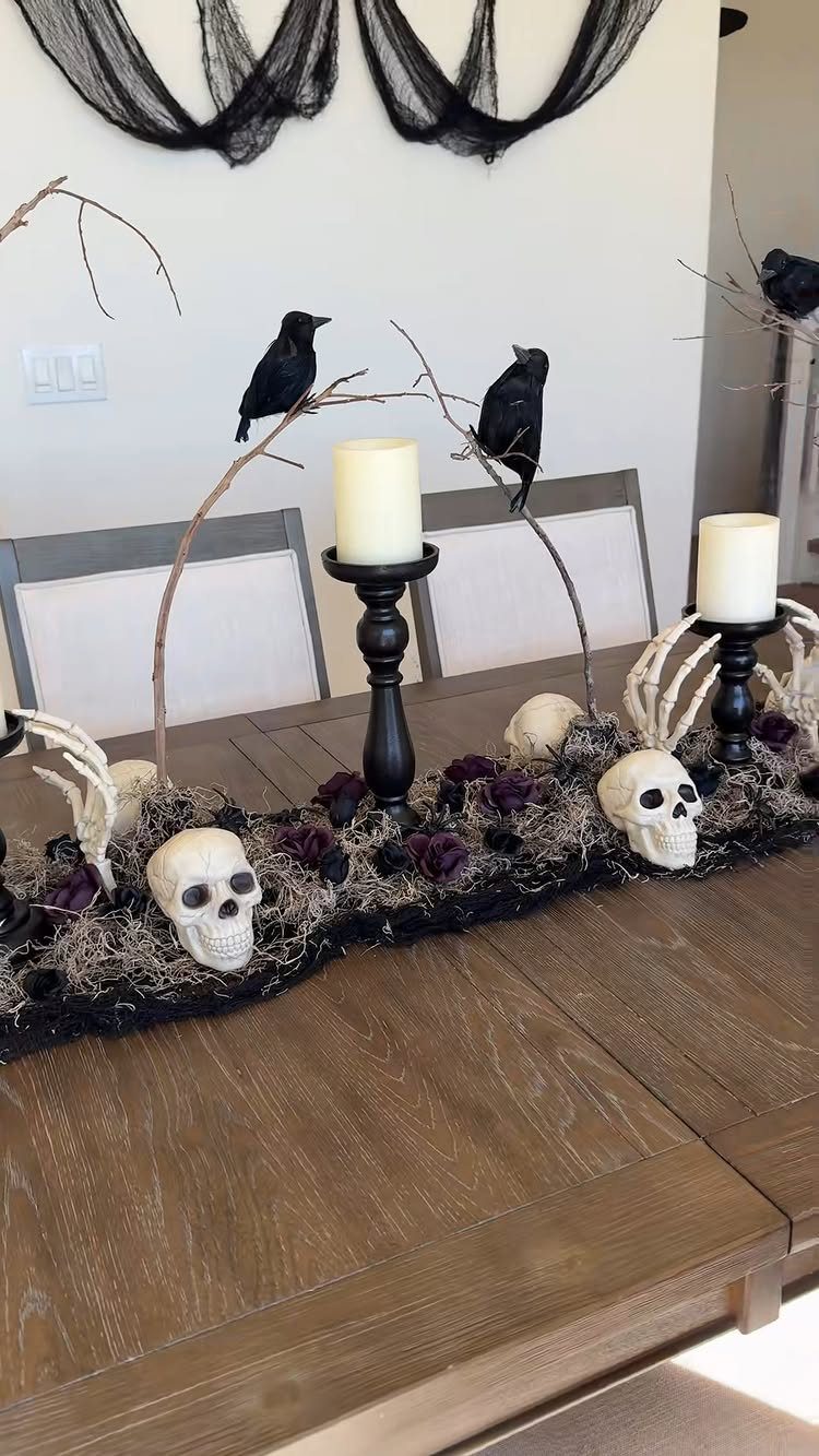 Halloween table runner with white skulls, skeletal hands, black candles, and black birds.