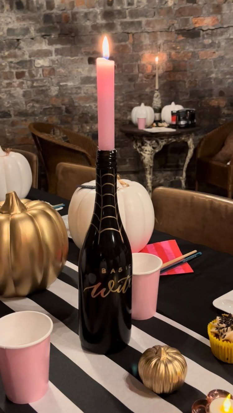 Black spray-painted wine bottle with gold spiderweb holding a pink taper candle.