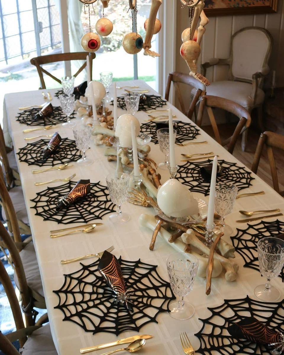 Black spiderweb placemats on a white table with gold cutlery and bone centerpieces.