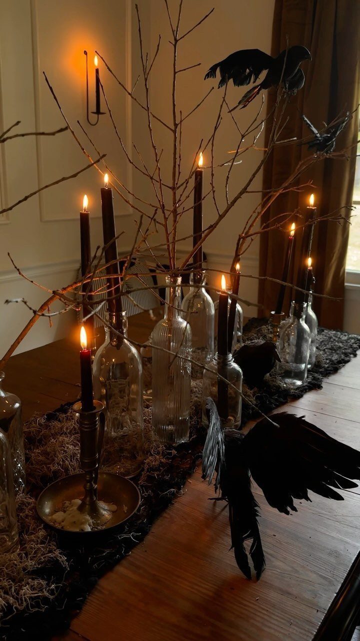 Clear glass wine bottles with branches and black candles on a spooky table.