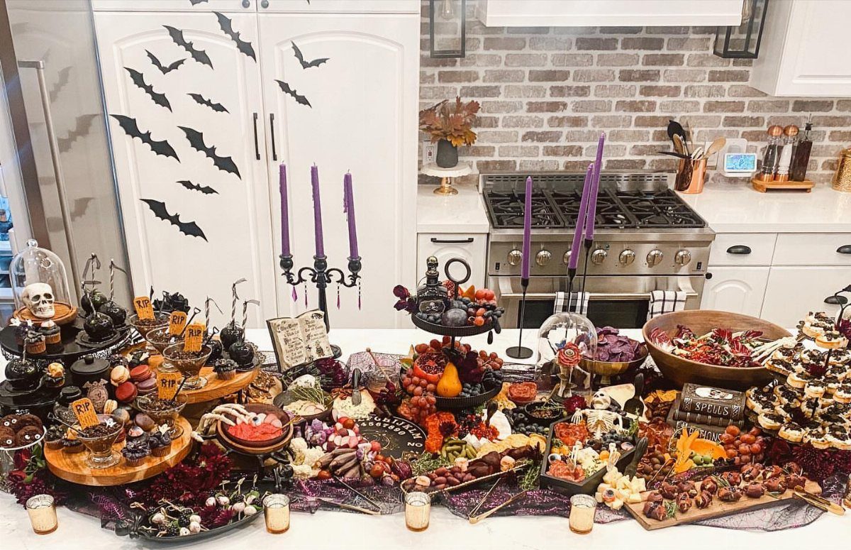 Halloween food spread with purple candles, a skull, and bat decorations in a kitchen.