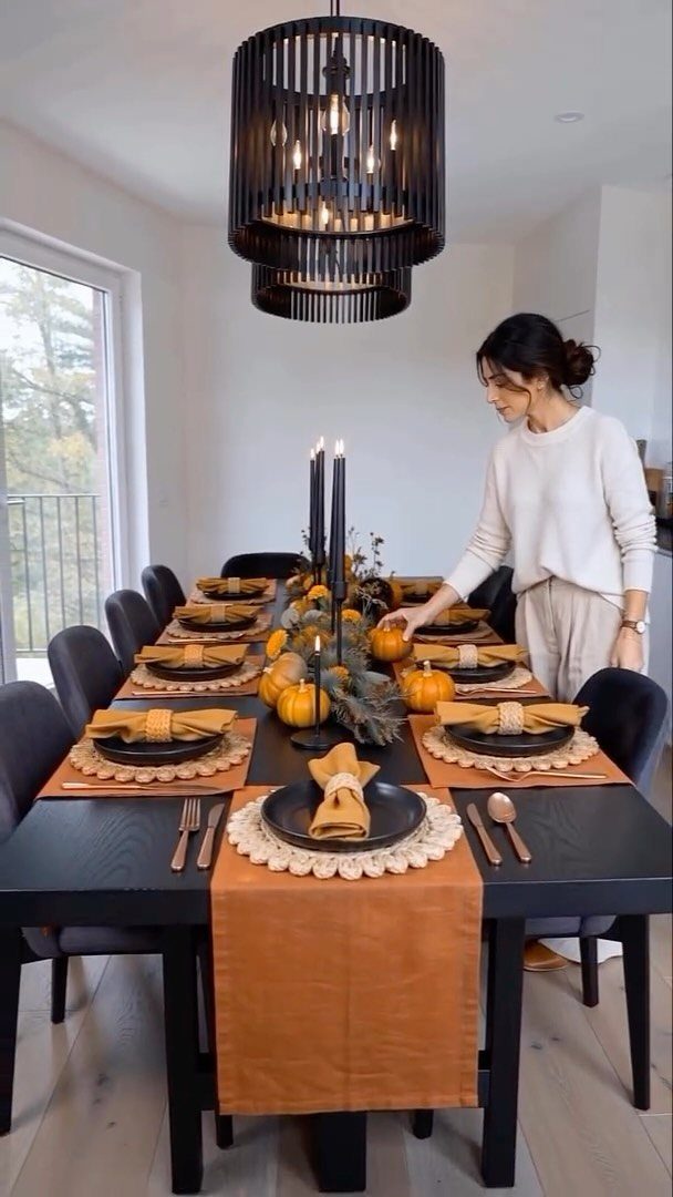 Woman arranging pumpkins on a black dining table with orange and black Halloween decor.