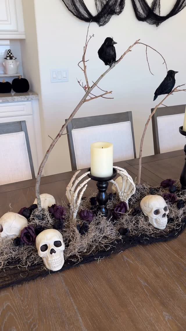 Halloween table centerpiece with skulls, black crows on branches, and a white candle.